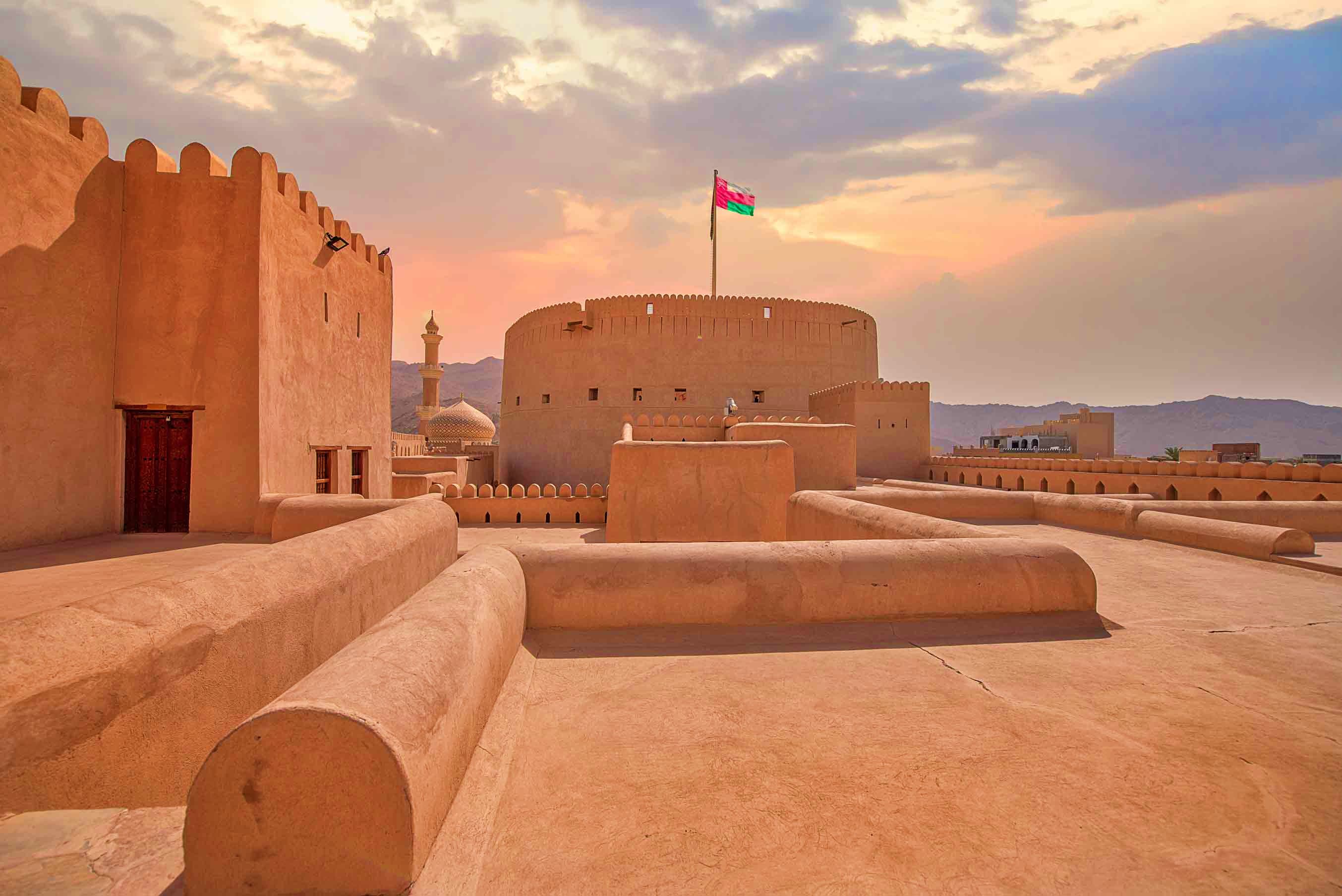 Historic Al Jalali Fort in Muscat, Oman with traditional adobe walls, cannons, and Omani flag at sunset